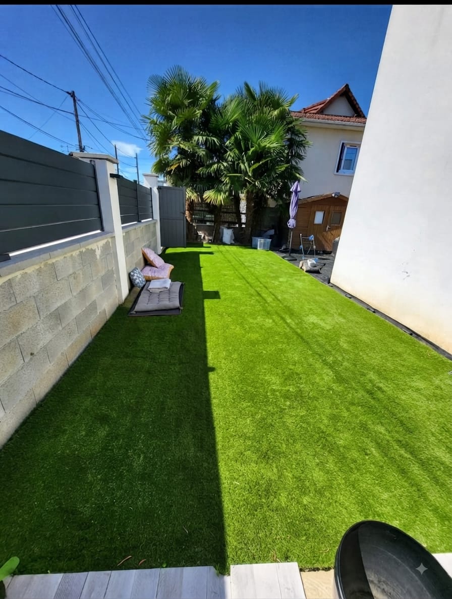 La même cour après pose : gazon synthétique continu jusqu’au mur, terrasse dégagée.