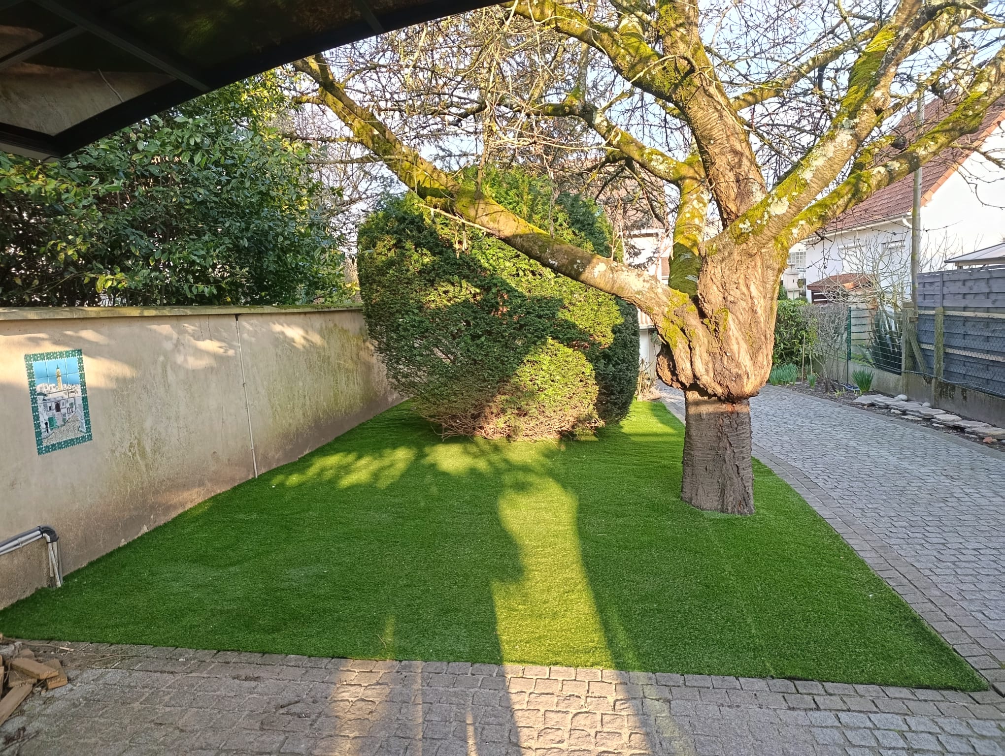 La cour entière en gazon synthétique, sous les arbres taillés.
